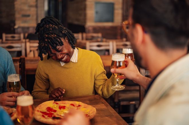 Friends laughing, drinking beer and eating pizza at a casual gathering in a pub or restaurant