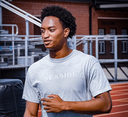 A young man wearing a "Seaside" t-shirt standing in front of a brick building.