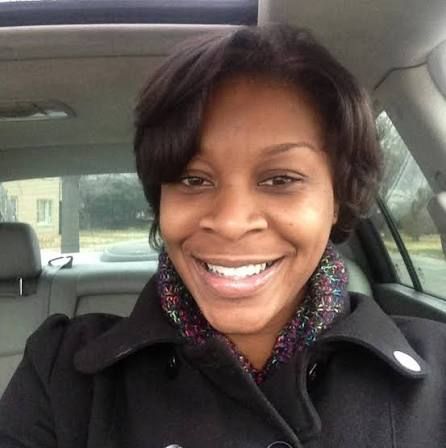 A smiling African American woman wearing a black coat and a colorful scarf in a car.