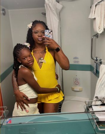 Two women, one wearing a yellow top and the other a white outfit, taking a selfie in a bathroom.