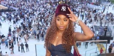 A young woman wearing a New York Yankees cap and crop top stands in a crowded stadium with a large audience visible in the background.