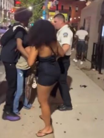 Two police officers restraining a person on the sidewalk of a city street at night.