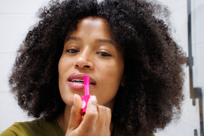 Young african american woman applying lip gloss in bathroom