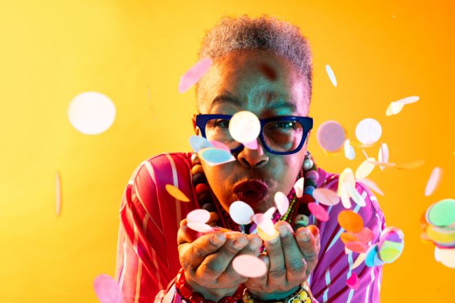 Senior woman celebrating birthday blowing colorful confetti