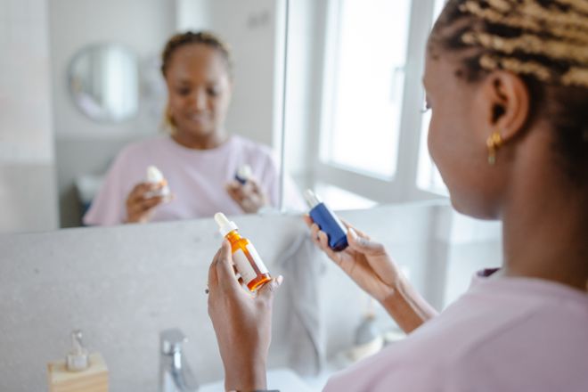 Woman holding facial serum in bathroom mirror during morning skincare routine