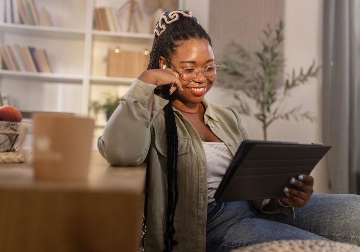 happy young black woman reading entertaining news on digital tablet at home