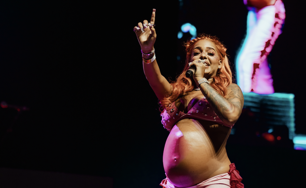 A woman in a pink outfit performing on stage, with her arms raised and a microphone in her hand.