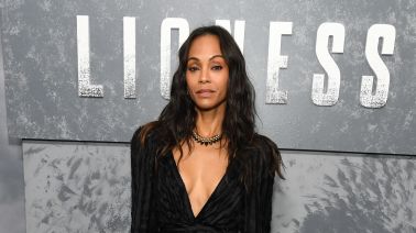 A woman in a black, ruched dress standing in front of a backdrop with the word "LIONESS" displayed prominently.