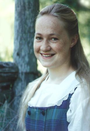 A smiling young woman with long blonde hair standing in front of a tree.