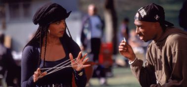 Two people, a woman with braided hair and a man wearing a cap, engaged in conversation outdoors.