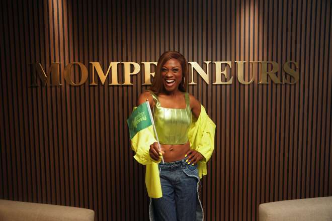 A smiling woman wearing a green crop top and yellow jacket stands in front of a sign that says "Entrepreneurs".