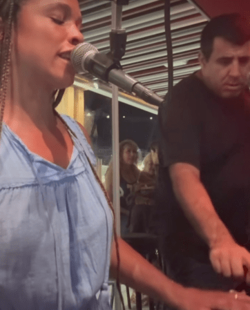 A woman singing into a microphone on a stage, with a man standing behind her.