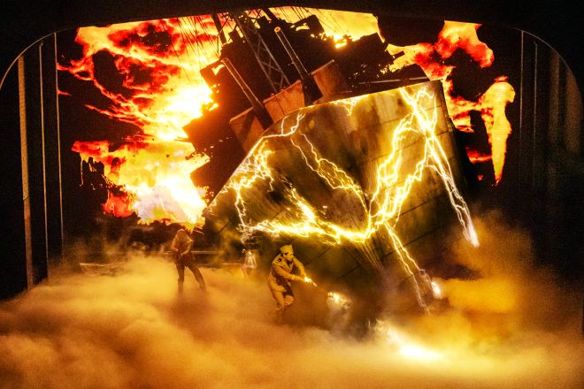 Dramatic explosion with intense flames, lightning, and silhouetted figures in a dark, fiery setting.