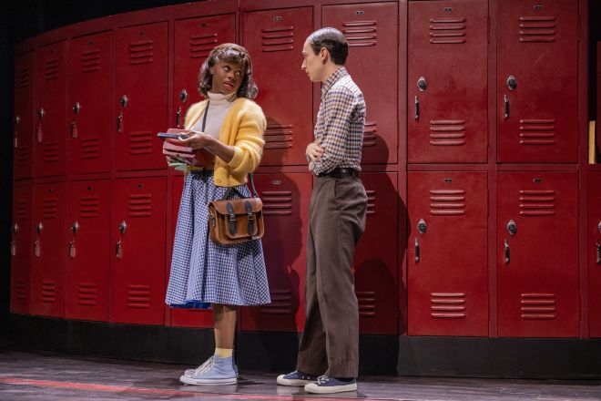 Two people, a woman and a man, standing in front of red lockers and conversing.