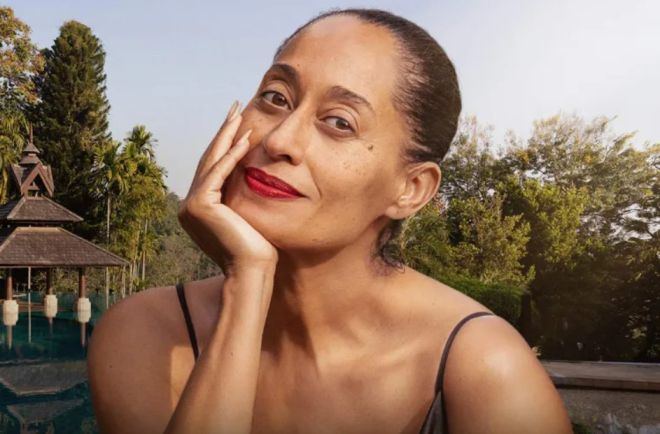 A woman with a serious expression resting her hand on her face, set against a backdrop of trees and a gazebo.