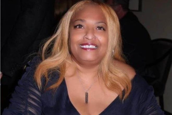 A smiling woman with long blonde hair wearing a black jacket and jewelry.