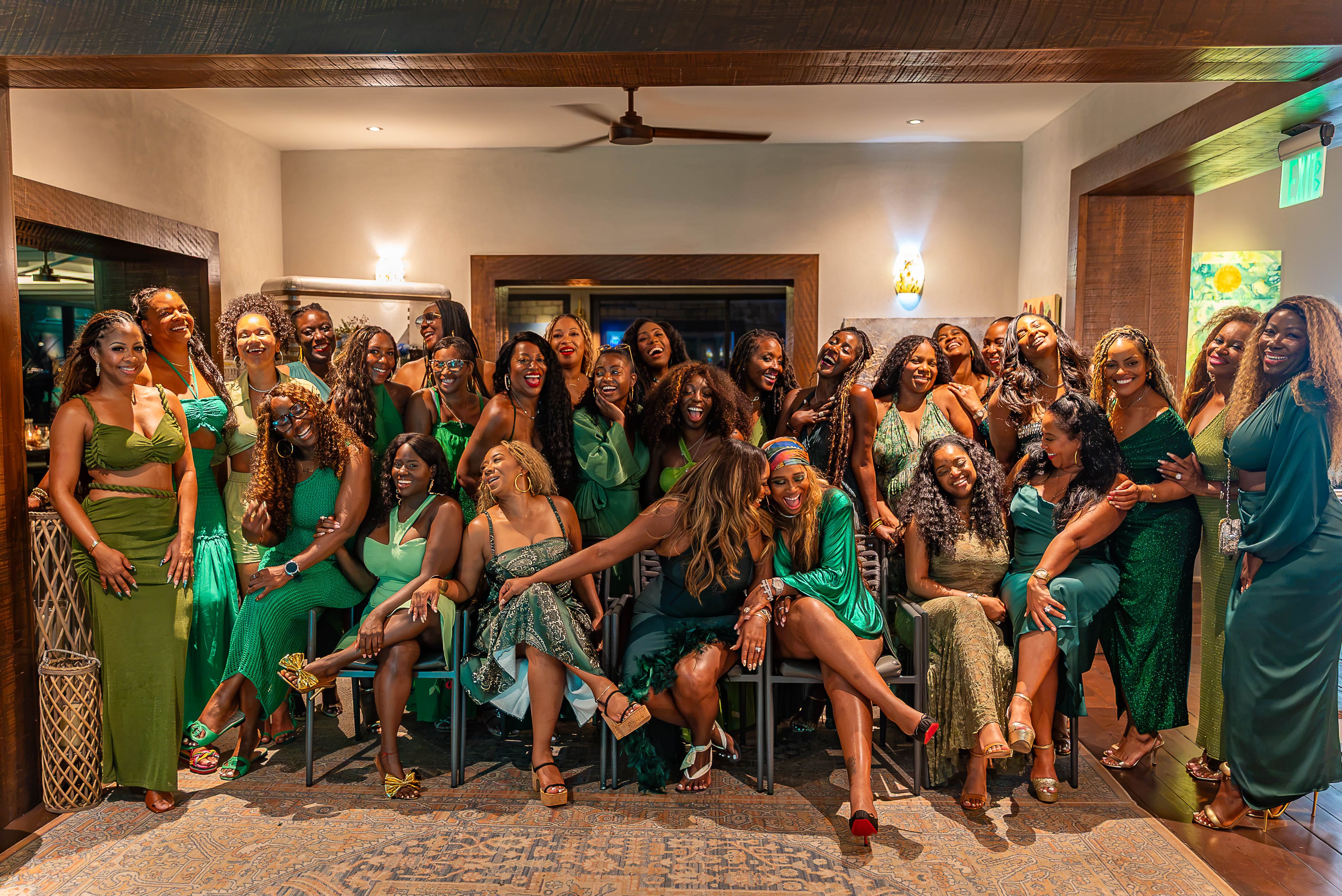 A large group of women wearing green and gold dresses and posing together in a festive indoor setting.