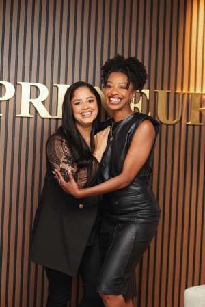 Two women embracing and smiling in front of a "Premiere" sign.