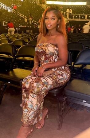 A woman in a strapless floral print jumpsuit sitting in a large arena with empty seats behind her.