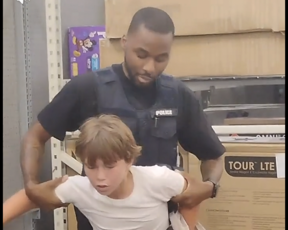 A police officer restraining a young person in what appears to be a school or office setting.