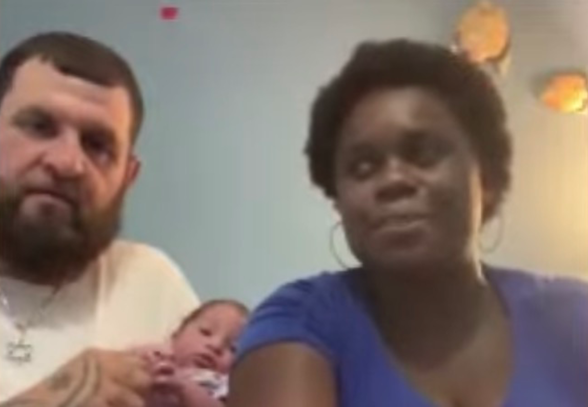 A man with a beard and a woman with short dark hair holding a newborn baby.