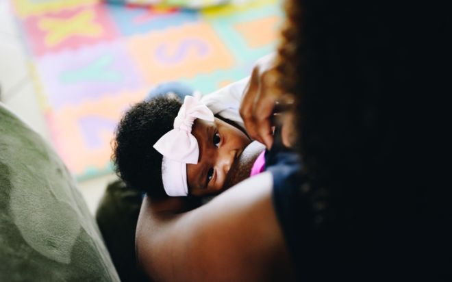 African American woman breastfeeds her 3 month old baby at home, motherhood